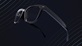A pair of black spectacles on a deep navy background with thin curving light blue lines, indicative of sound waves 