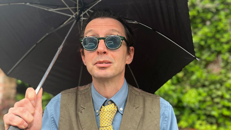 Man holding an umbrella wearing round black sunglasses
